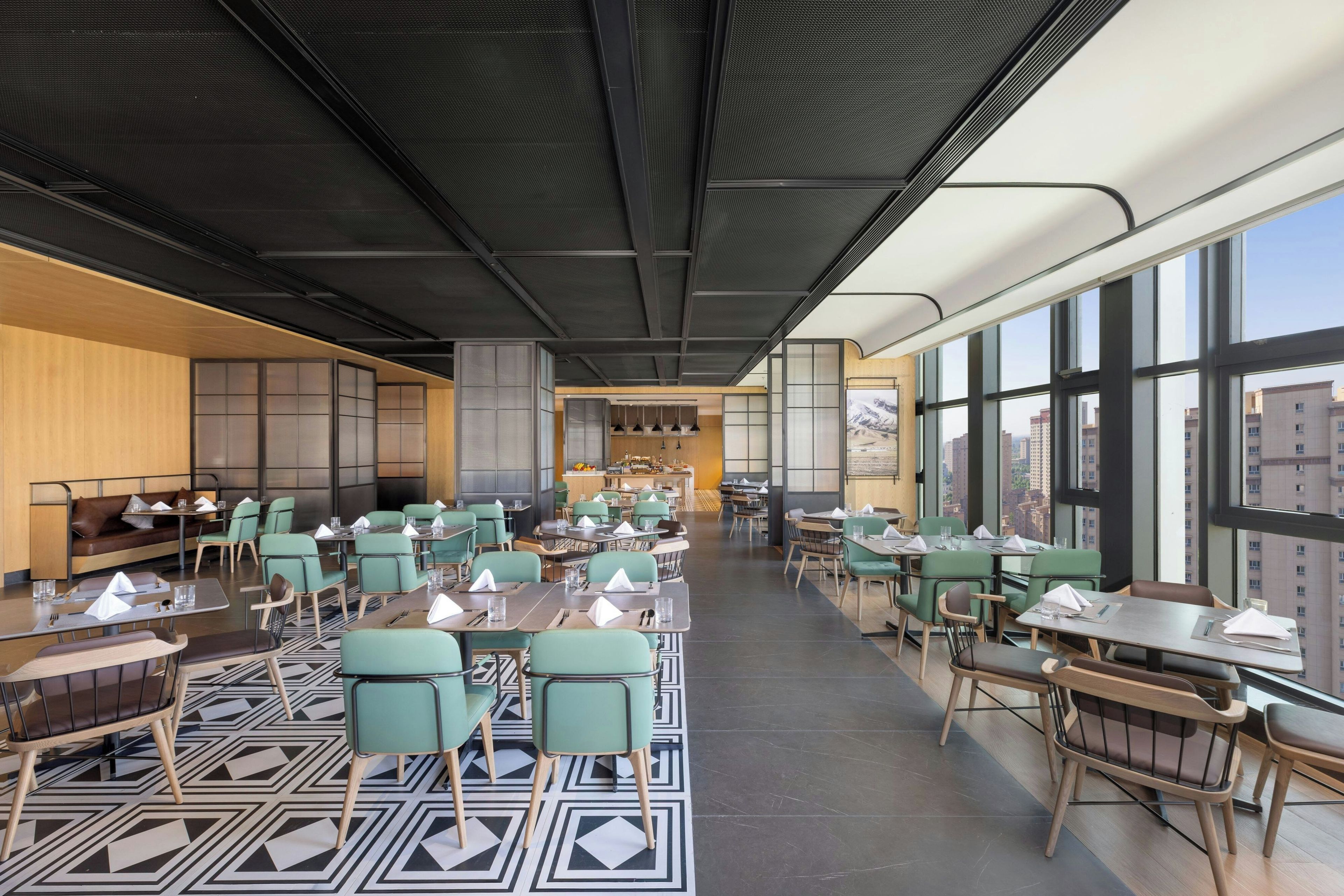 Un restaurant spacieux avec de hauts plafonds, un mobilier moderne et de grandes fenêtres offrant une vue sur la ville.