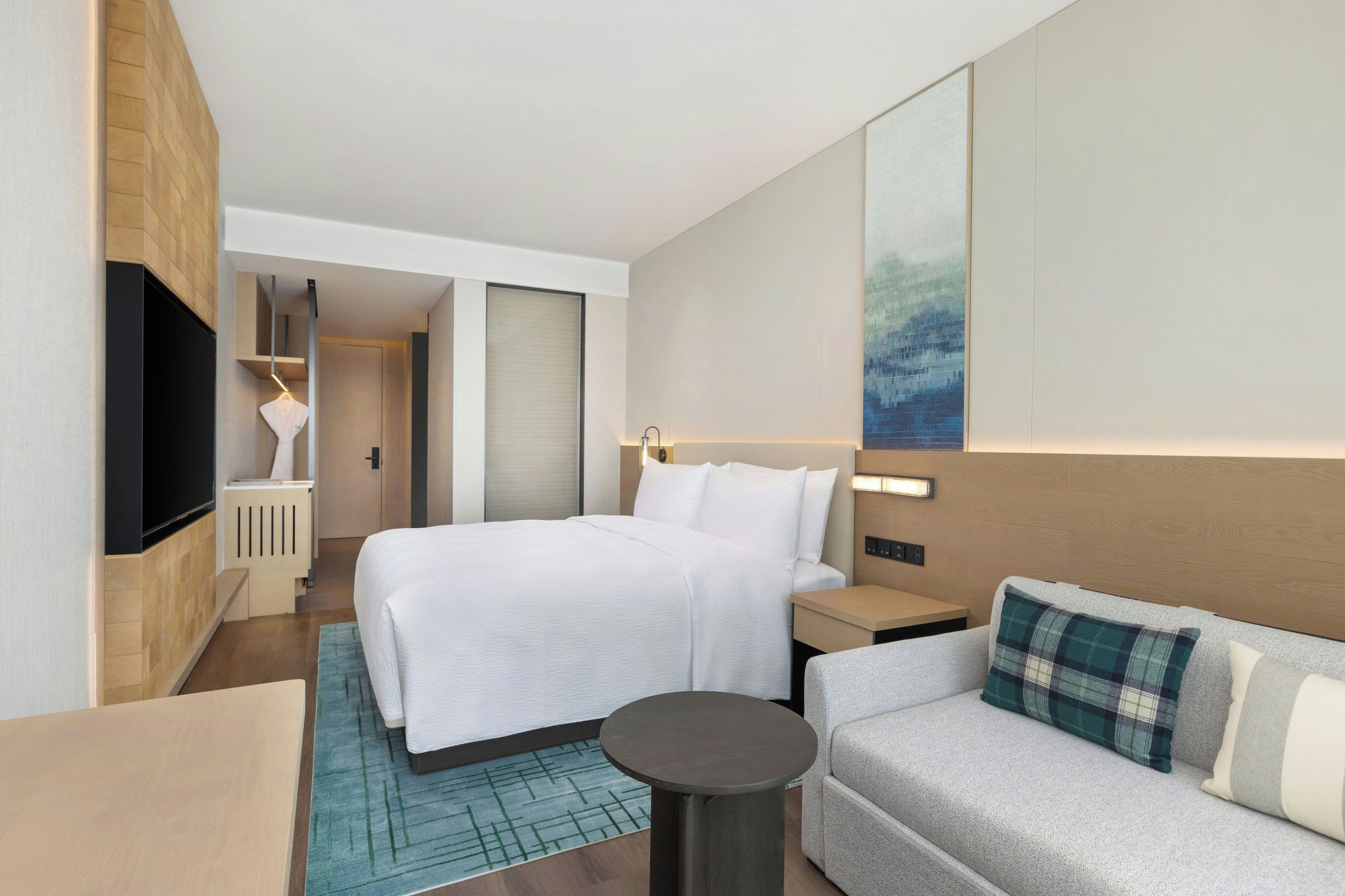 A hotel room with a bed, a sofa, a TV, and a painting on the wall.