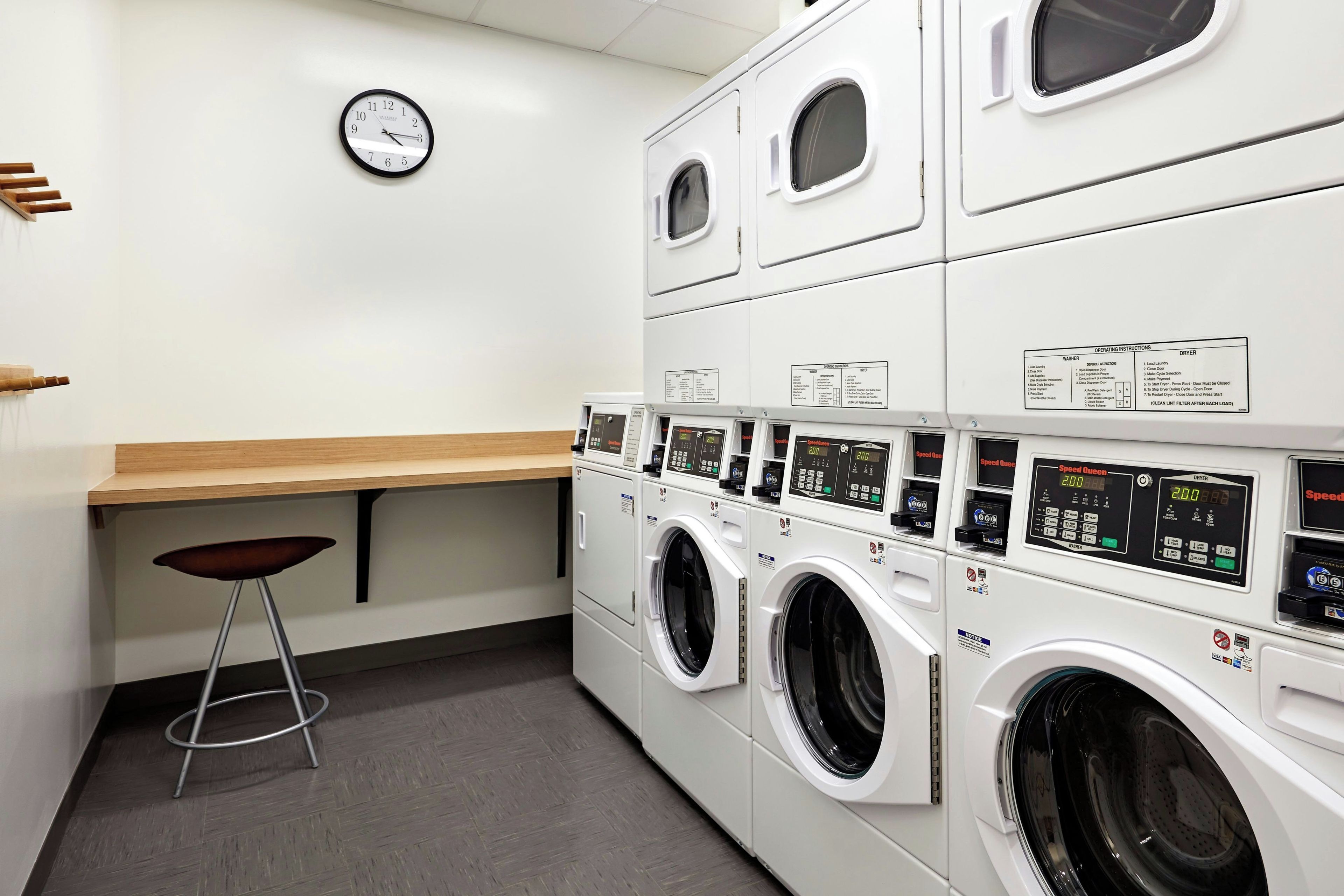 A laundry facility with multiple washing machines, a wooden counter, and a wall clock.