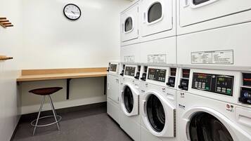 A laundry facility with multiple washing machines, a wooden counter, and a wall clock.