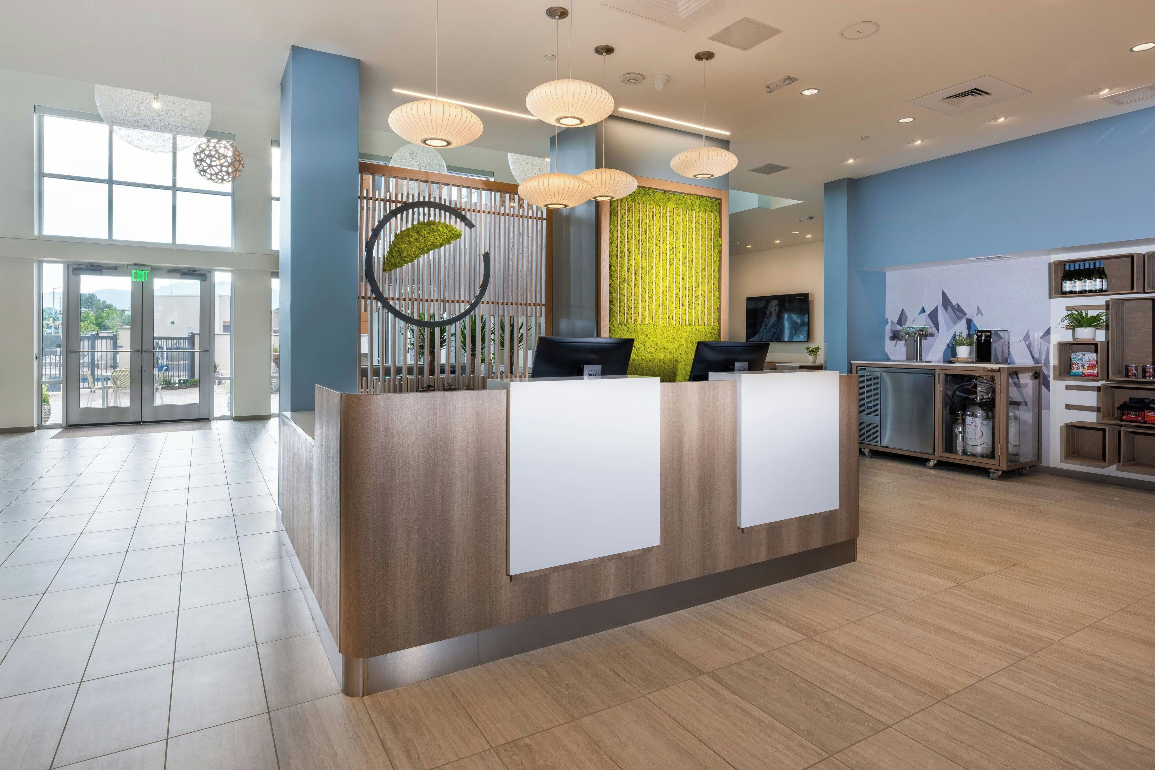 A modern reception desk with a wooden finish, a green vertical garden, and a large window providing natural light.