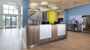 A modern reception desk with a wooden finish, a green vertical garden, and a large window providing natural light.