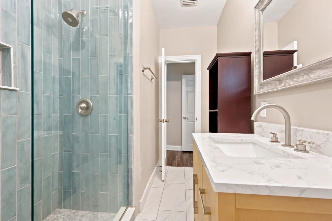 A modern bathroom with a glass shower enclosure, a marble sink, and a wooden vanity.