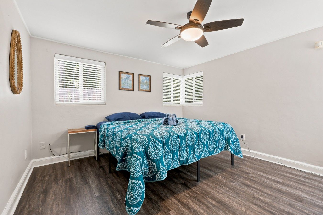 A bedroom with a bed, a ceiling fan, and two windows with blinds.