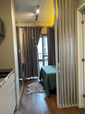 A bedroom with a bed, curtains, a window, and a view of the outside. - Modern studio in the city center | Pool + Gym | Subway (São Paulo)