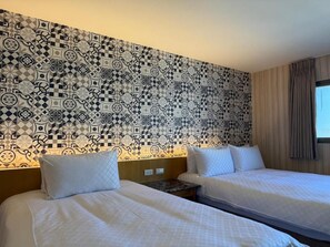 Habitació d'hotel amb dos llits, un mur amb un disseny i una finestra amb cortines.