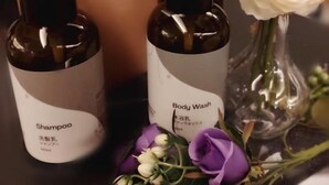 Duas garrafas de shampoo e líquido de banho com etiquetas em língua estrangeira, ao lado de um vaso com flores.