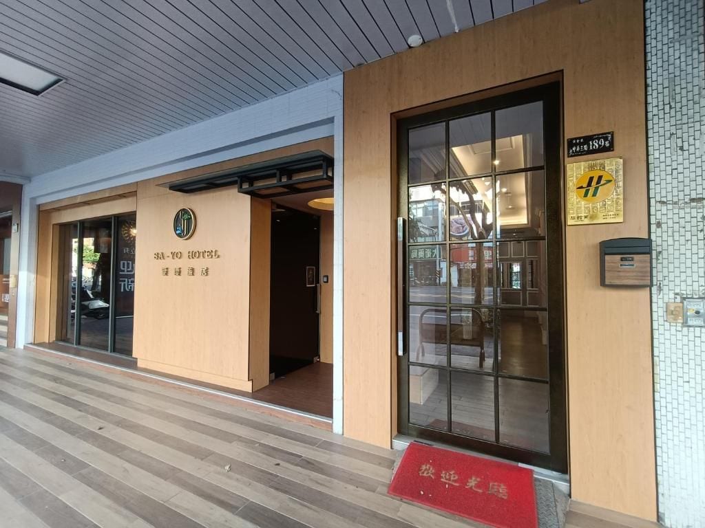 A hotel entrance with a wooden facade, a glass door, and a red mat at the entrance.