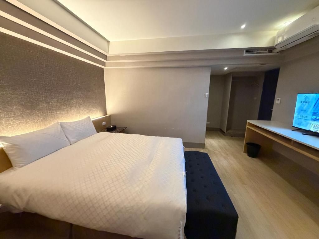 Habitación de hotel con una cama grande, una mesita de noche, un escritorio con computadora y una pequeña zona de estar.