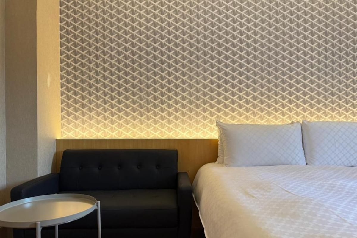 Habitació d'hotel amb un llit, una butaca negra i una taula rodona petita.