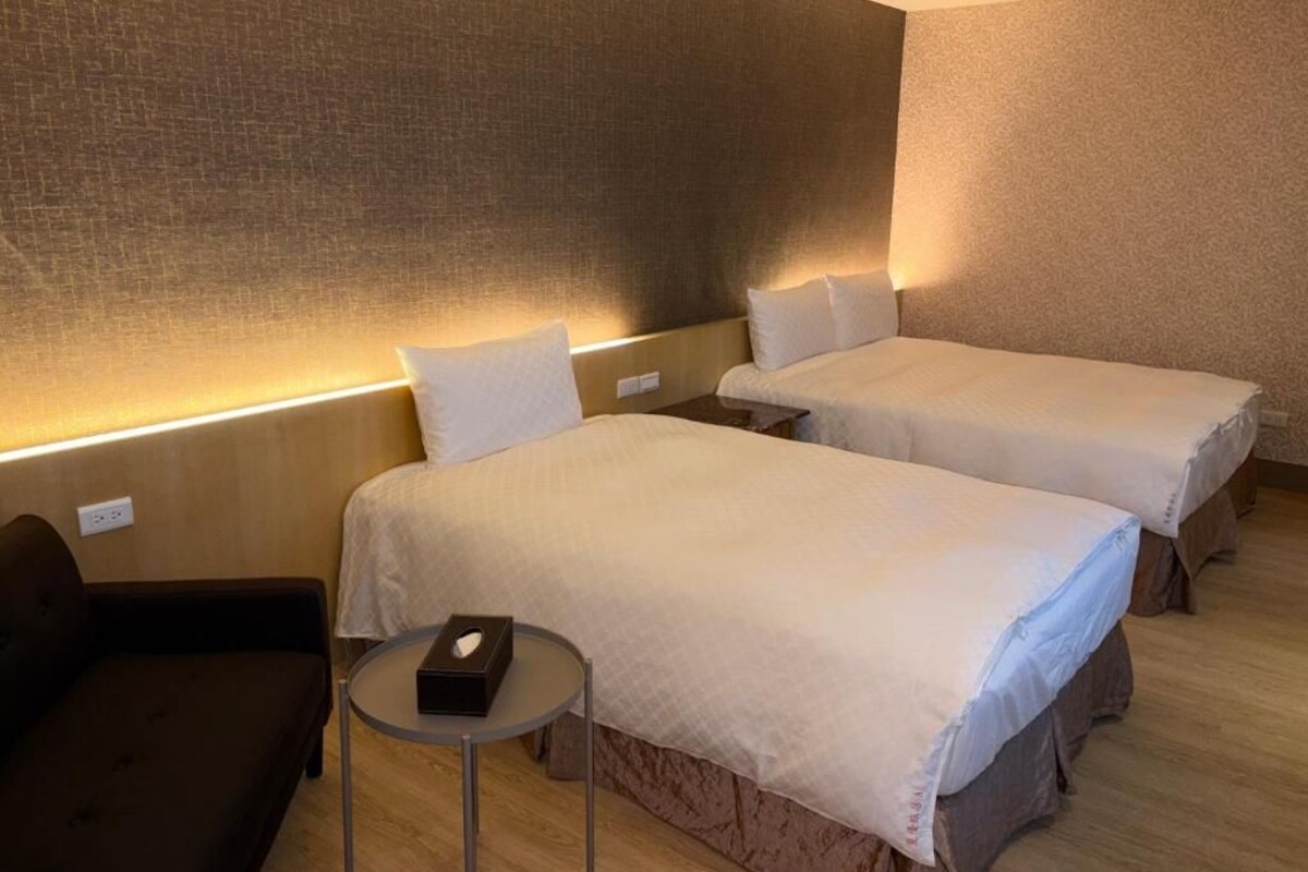 Habitació d'hotel amb dos llits, una taula petita i un sofà.