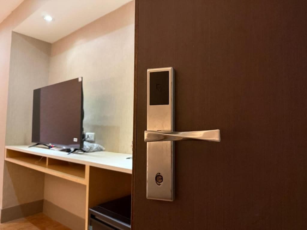 Quarto de hotel moderno com porta de madeira, escrivaninha embutida e uma tela pequena na porta.