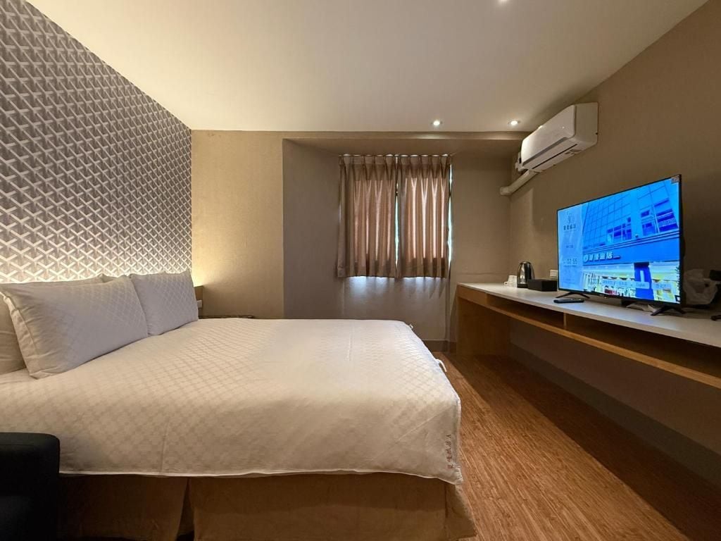 A hotel room with a bed, a TV, a desk, and a window with curtains.