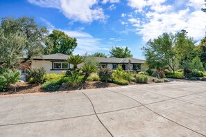 A residential property with a paved driveway, a two-story house, and a well-maintained garden with various plants and shrubs.