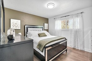 A modern bedroom with a bed, bedside table, and a window with curtains.