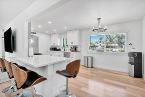 A modern kitchen with white cabinetry, a central island, bar stools, and a large window with a view.