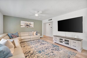 A living room with a beige sectional sofa, a patterned rug, a flat-screen TV, and a white entertainment unit.