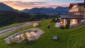 A residential area with a house, a paved path, a small pond, and a mountain backdrop. - Charming 2-Bedroom Chalet at Stabingerhof Farm, South Tyrol (Trentino-Alto Adige)