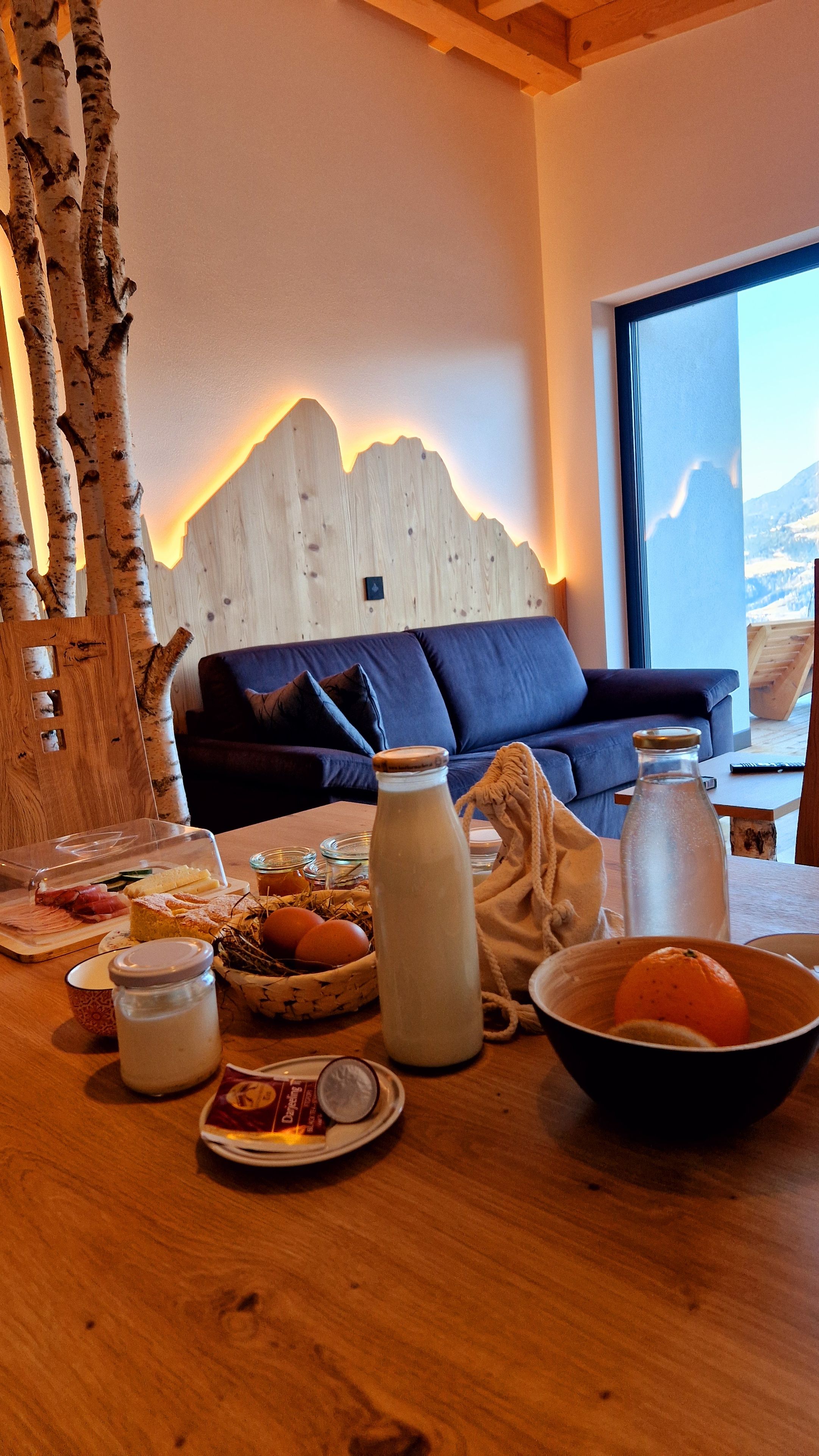 Een gezellige woonkamer met een houten accentmuur, een bank en een eettafel met eten erop.