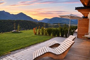 A wooden deck with lounge chairs and a table, overlooking a grassy field and mountains. - Charming 2-Bedroom Chalet at Stabingerhof Farm, South Tyrol (Trentino-Alto Adige)