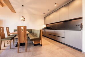 Una cucina moderna con angolo pranzo integrato, caratterizzata da un tavolo da pranzo in legno con sedie, una panca imbottita verde e illuminazione a incasso.