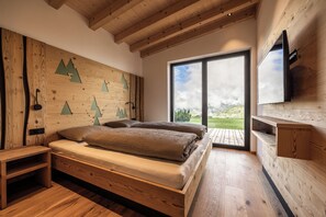A bedroom with a wooden headboard, a bed with two pillows, a wooden nightstand, a TV mounted on the wall, and a large window with a view of the outdoors. - Charming 2-Bedroom Chalet at Stabingerhof Farm, South Tyrol (Trentino-Alto Adige)