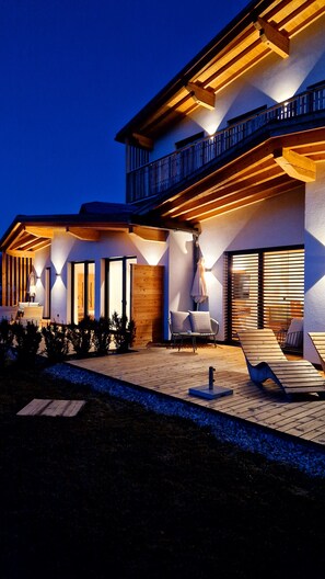 Ein modernes Haus mit Balkon, Sitzgelegenheit im Freien und einer gut beleuchteten Eingangsparte.