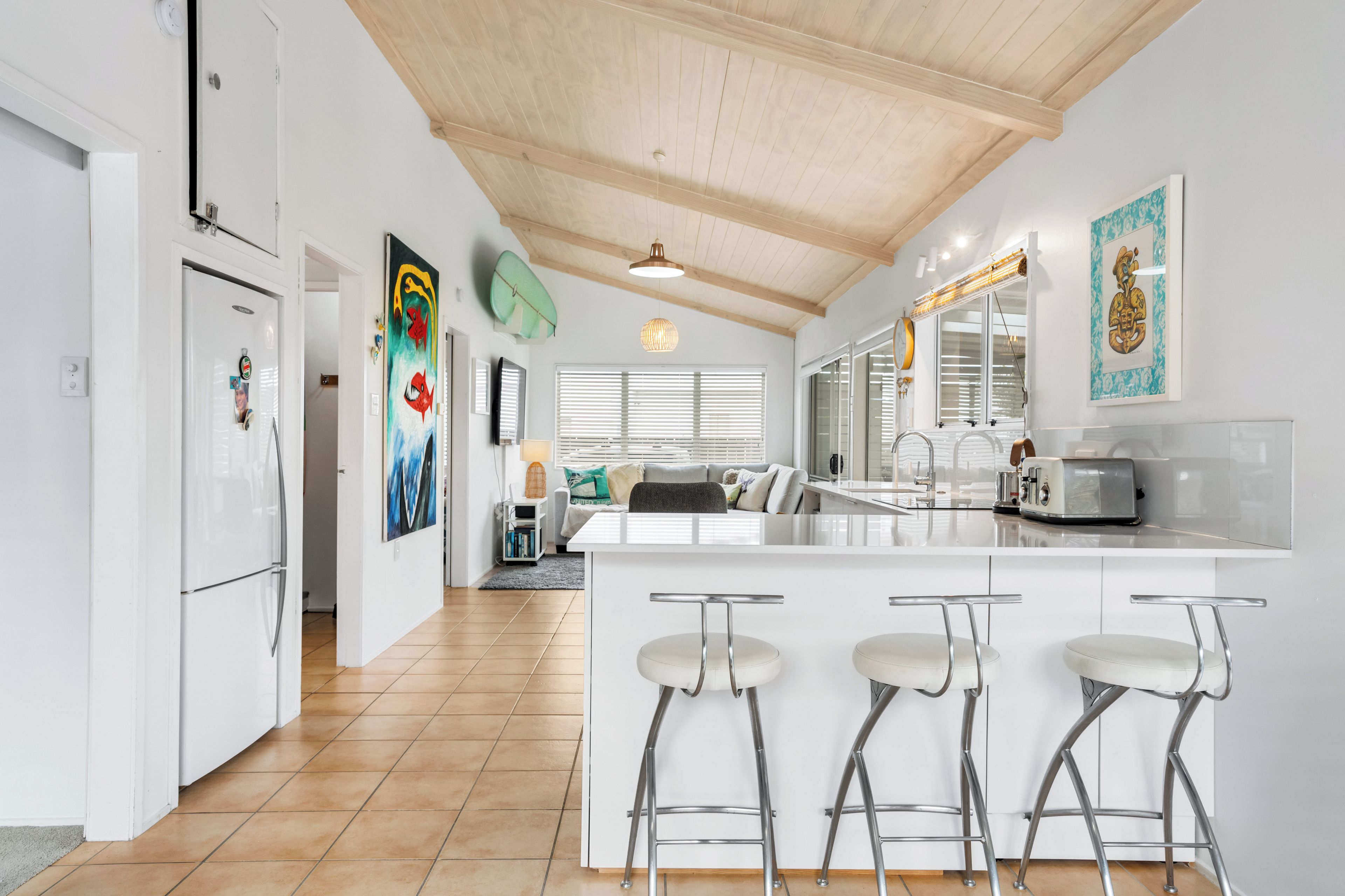 Een moderne keuken met een houten plafond, witte kasten en een bar met krukken.