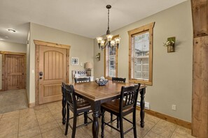 A dining room with a wooden table and chairs, a chandelier, and a door with a sign. - Buffalo Peaks - Where your Adventure Begins (Driggs)