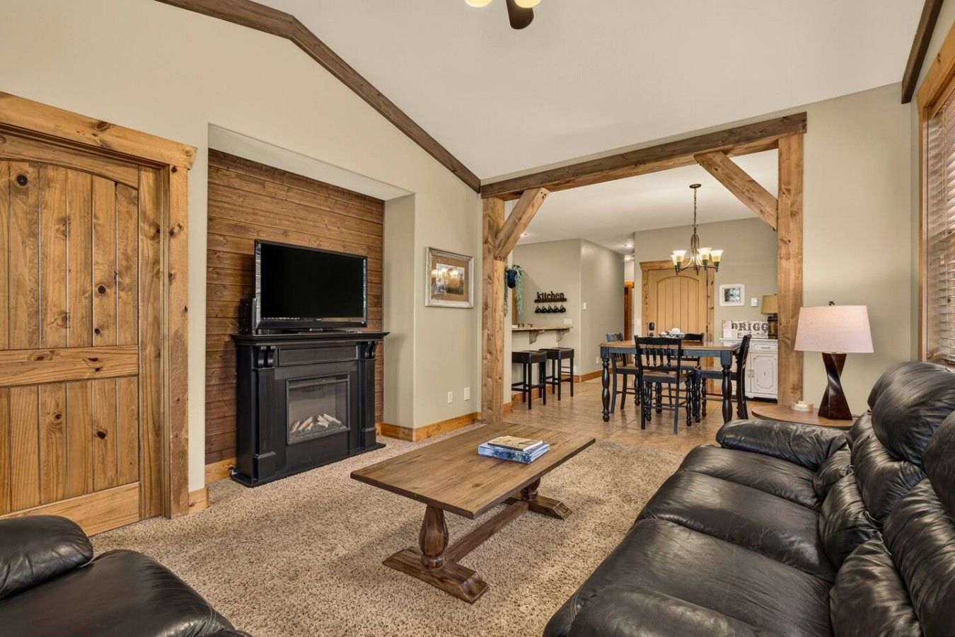 A living room with a fireplace, a television, a sofa, and a dining area with a kitchen in the background.