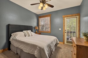 A bedroom with a bed, a nightstand, a lamp, a ceiling fan, and a door with a window. - Buffalo Peaks - Where your Adventure Begins (Driggs)