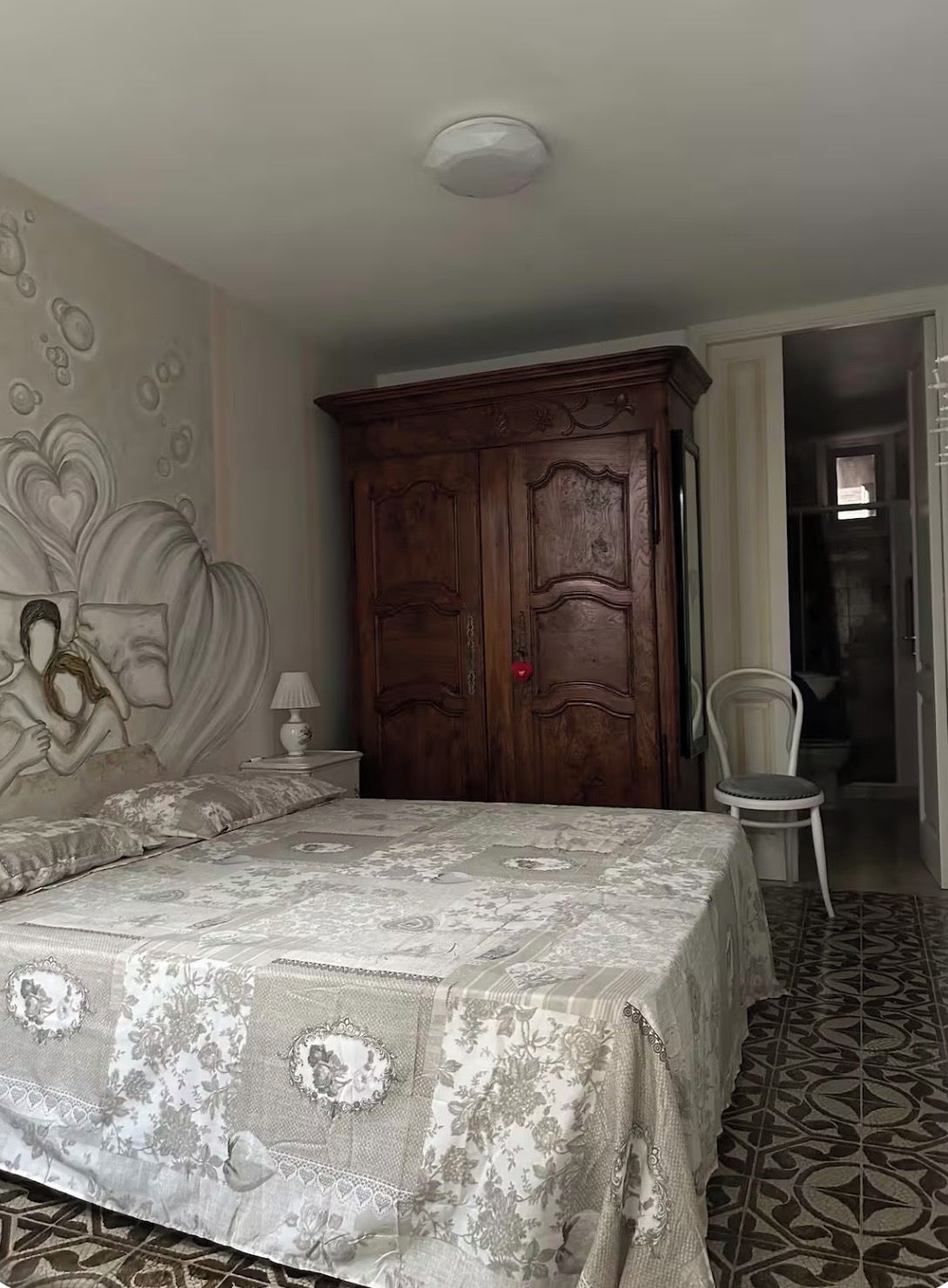 A bedroom with a bed, a wardrobe, a chair, and a wall with a floral pattern.