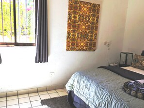 Ein Schlafzimmer mit einem Bett, einem Wandbild, einem Fenster mit Vorhängen und einem gefliesten Boden.