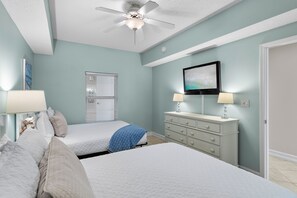 Ein Schlafzimmer mit zwei Betten, einem Deckenventilator, einer Kommode und einem an der Wand befestigten Fernseher.