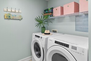 Ein Waschbereich mit zwei Frontlader-Waschmaschinen, einem Wäscheständer, einem an der Wand befestigten Regal mit gefalteter Kleidung und einer Wanddekoration.