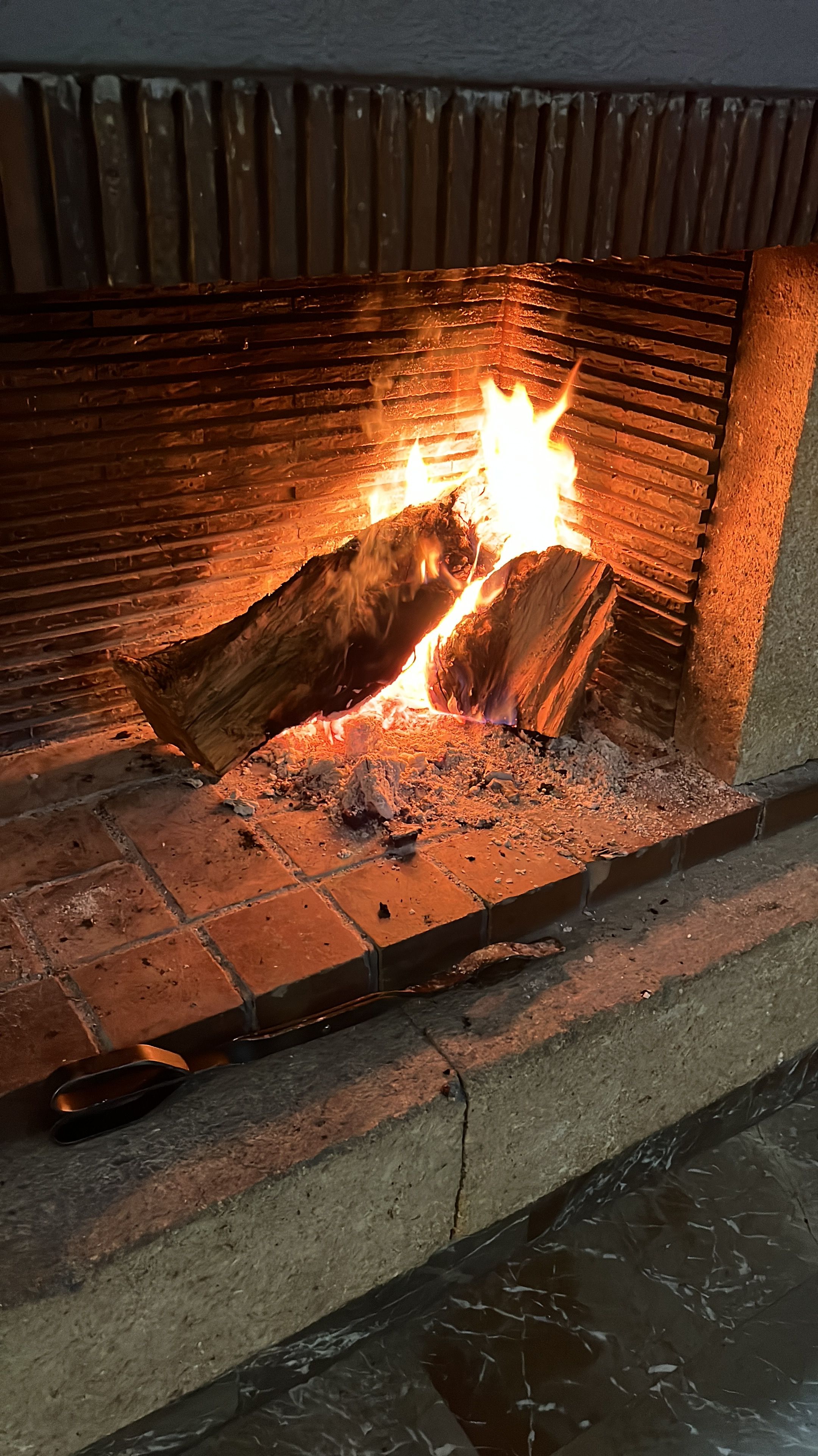 A fireplace with burning logs, a brick floor, and a stone wall.