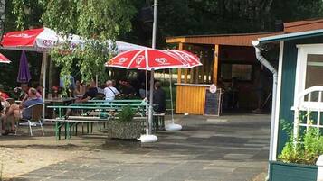 En udendørs spiseplads med borde, stole, parasoller og en bygning i baggrunden.