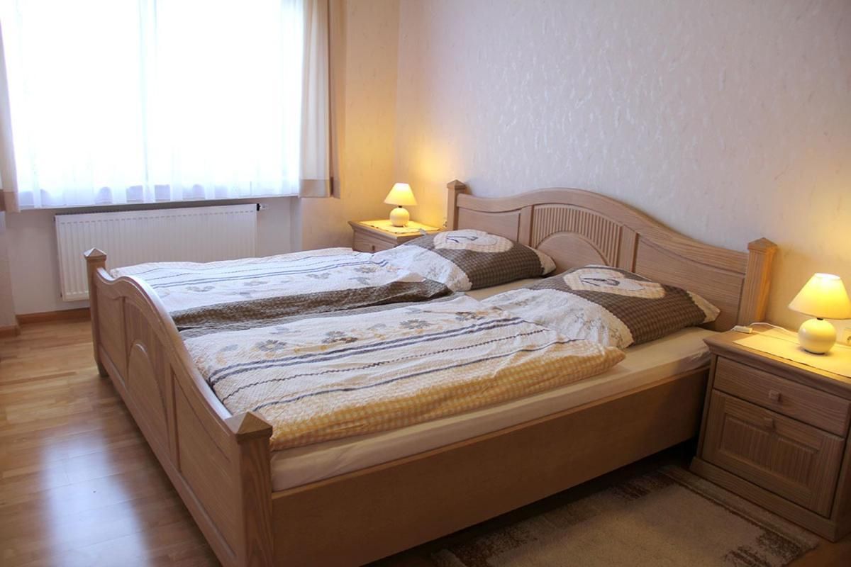Un lit double avec un cadre en bois, deux tables de chevet avec des lampes, un radiateur et une fenêtre avec des rideaux.