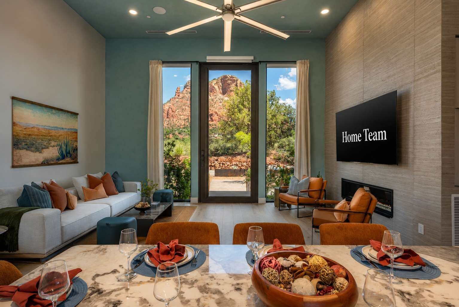 A modern living room with a sofa, armchairs, a dining table set for two, and a television mounted on the wall.
