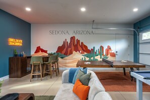 Een kamer met een pooltafel, een muurschildering van Sedona, Arizona, en een neonbord.