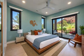 Ein Schlafzimmer mit einem großen Bett, zwei Nachttischen, einem Deckenventilator und Blick auf eine natürliche Landschaft durch eine Glasschiebetür.
