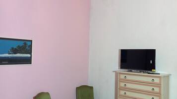 Una habitación con dos sillas verdes, un televisor sobre una cómoda y una araña.