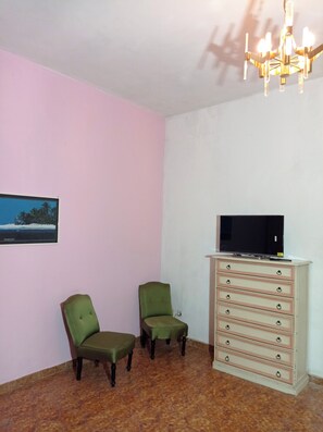 A room with two green chairs, a television on a dresser, and a chandelier.