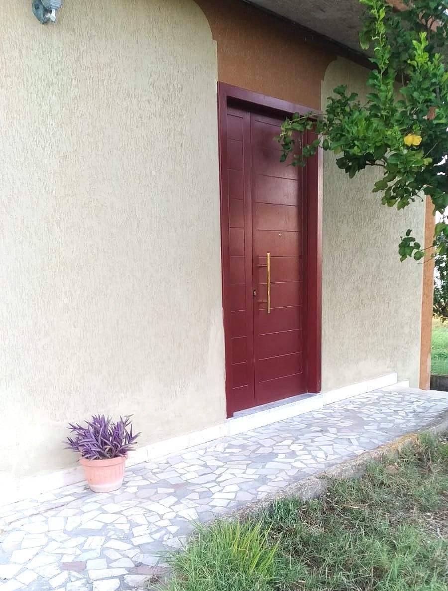 A building with a red door, a potted plant, and a tiled walkway.