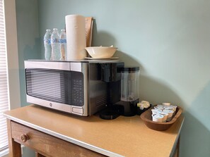 Une petite cuisine équipée d’un four à micro-ondes, d’une machine à café et d’un bol rempli de pots de yaourt, le tout posé sur un comptoir en bois.