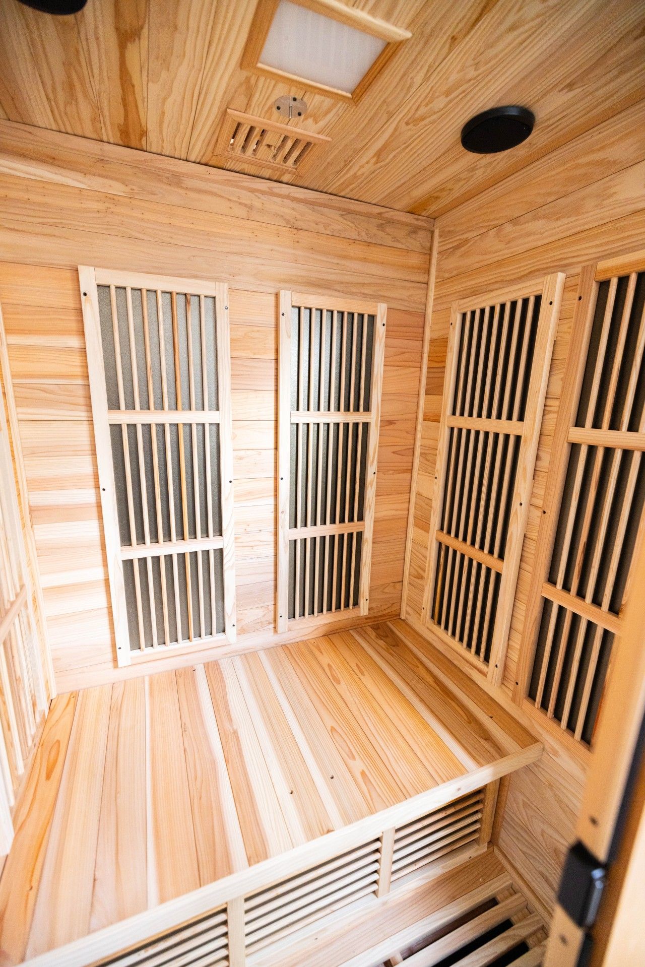 Un sauna avec des parois en lattes de bois et une bouche d’aération au plafond.