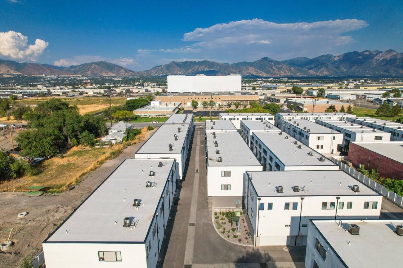 Un ensemble immobilier moderne composé de plusieurs bâtiments à toits plats, doté d’un espace central ouvert et surplombé par un paysage montagneux.