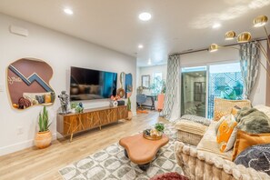Un salon moderne avec un téléviseur à écran plat, une console en bois et un canapé agrémenté de coussins à motifs.
