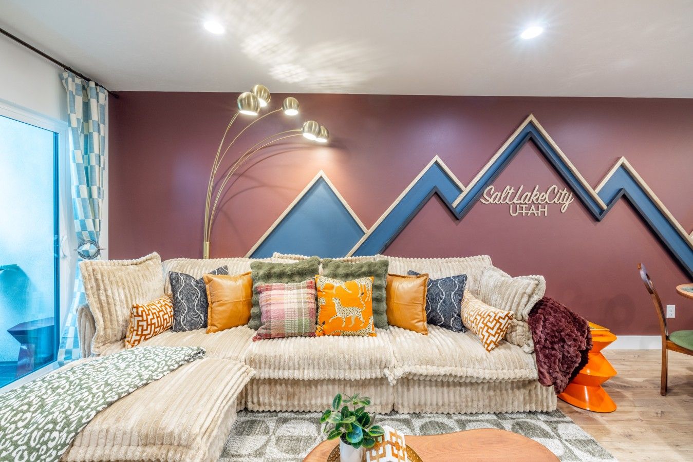 A modern living room with a sectional sofa, decorative pillows, a wall-mounted light fixture, and a geometric wall design.