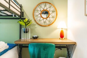 Une chambre d’hôtel avec un lit superposé, un bureau avec une lampe, une plante en pot et un miroir décoratif.